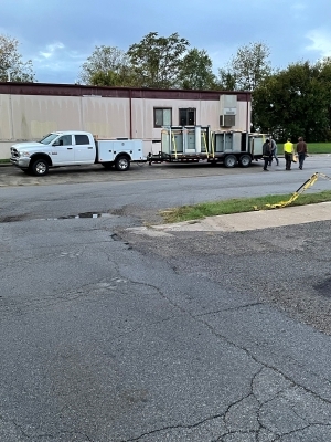 Truck pulling a trailer with workers walking by it.