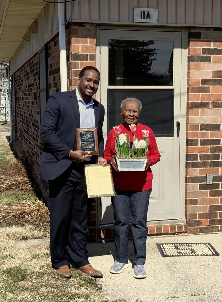 Keon standing with Frances Sanders, presenting her a plaque and flowers.